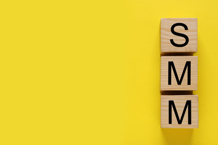 Cubes with abbreviation SMM (Social media marketing) on yellow background, flat lay. Space for text
