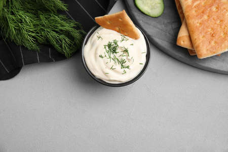 Tasty creamy dill sauce, crackers and ingredients on gray table, flat lay. Space for text