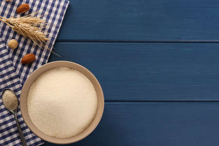 Uncooked organic semolina with spikelets and nuts on blue wooden table, flat lay. Space for text