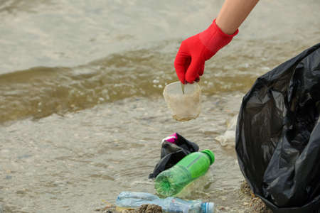 Woman in gloves with trash bag collecting garbage on beach, closeup