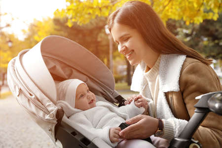 Happy mother with her baby daughter in stroller outdoors on autumn day
