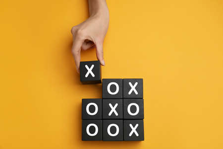 Woman playing tic tac toe game on yellow background, top view