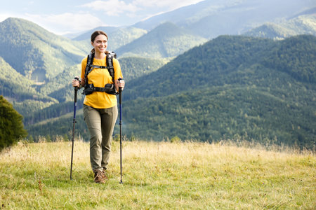 Woman with backpack and trekking poles hiking in mountains. Space for text