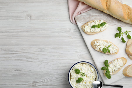 Bread with cottage cheese and basil on white wooden table, flat lay. Space for textの写真素材