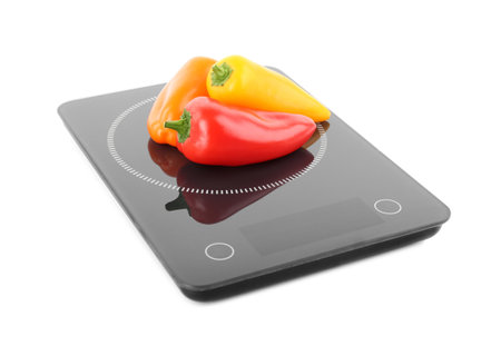 Heap of ripe bell peppers on kitchen scales against white background