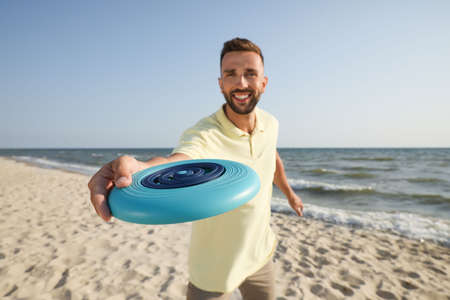Happy man throwing flying disk at beach, focus on handの写真素材