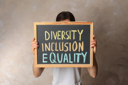 Woman holding chalkboard with text Diversity Inclusion Equality on beige backgroundの写真素材