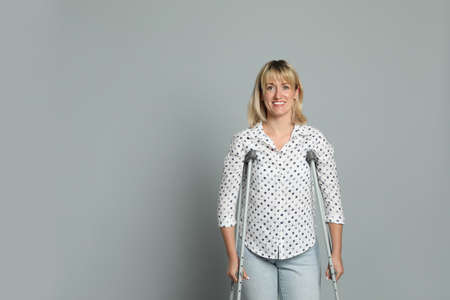 Portrait of happy woman with crutches on gray background. Space for textの写真素材