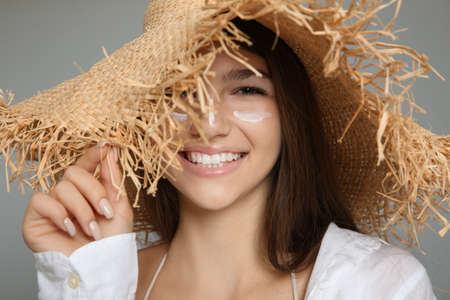 Teenage girl with sun protection cream on her face against gray background