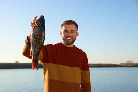 Fisherman holding caught fish at riverside. Recreational activity