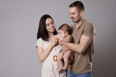 Happy family. Couple with their cute baby on gray background