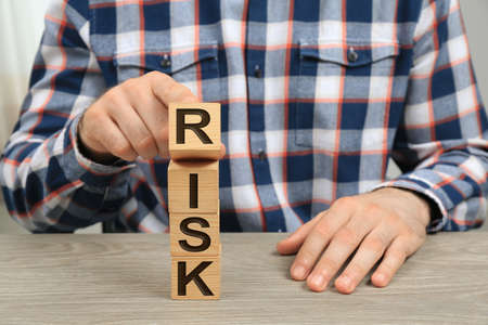 Man destroying tower of cubes with word Risk at table, closeupの写真素材