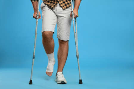 Young man with injured leg using axillary crutches on light blue background, closeupの写真素材