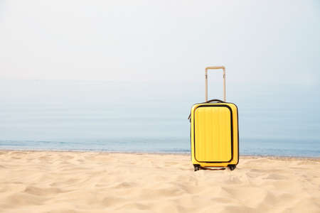 Yellow suitcase on sandy beach, space for textの写真素材