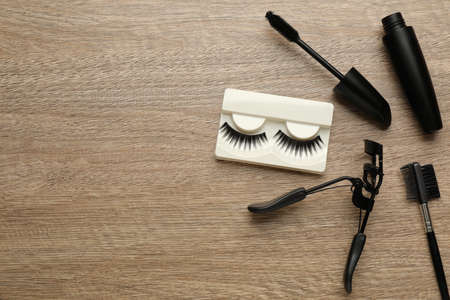 False eyelashes, curler, brush and mascara on wooden table, flat lay. Space for textの写真素材