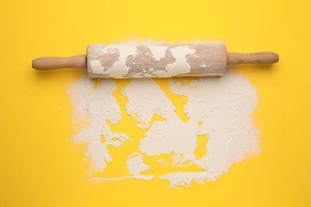 Wooden rolling pin and flour on yellow background, top view. Space for textの写真素材