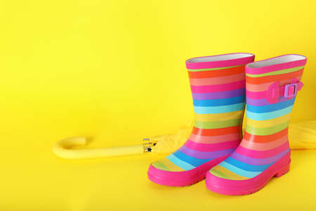 Pair of striped rubber boots near umbrella on yellow background. Space for textの写真素材