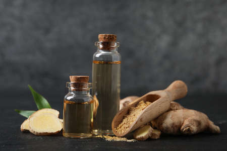 Glass bottles of essential oil, ginger powder and root on dark tableの写真素材