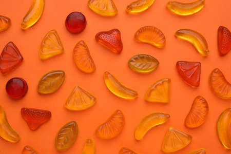 Delicious gummy fruit candies on orange background, flat layの写真素材