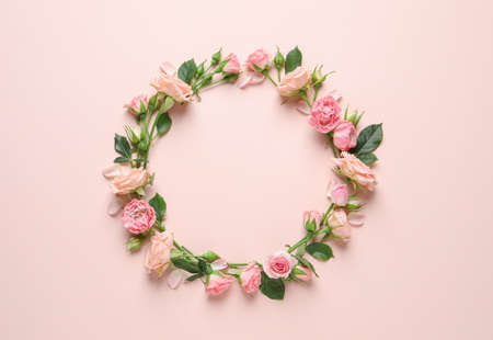 Wreath made of beautiful flowers and green leaves on pale pink background, flat lay. Space for textの写真素材