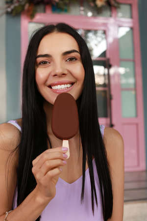 Beautiful young woman holding ice cream glazed in chocolate on city street