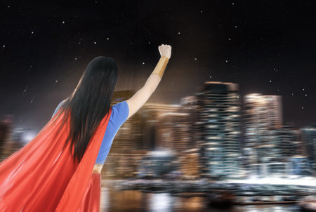 Young woman wearing superhero costume and beautiful cityscape in night on backgroundの写真素材