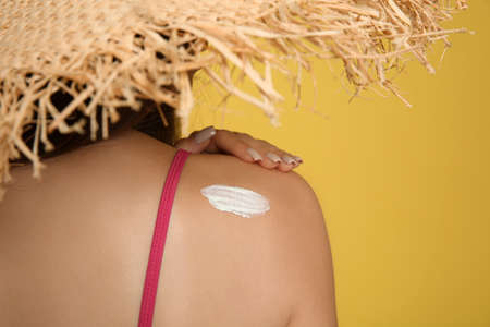 Teenage girl with sun protection cream on her back against yellow background, closeup