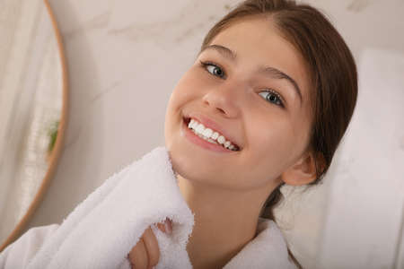 Beautiful teenage girl wiping face with towel at home, closeupの写真素材