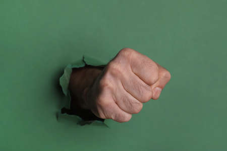 Man breaking through green paper with fist, closeupの写真素材