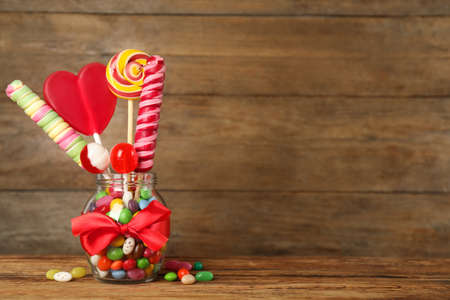 Jar with different delicious candies on wooden table, space for text