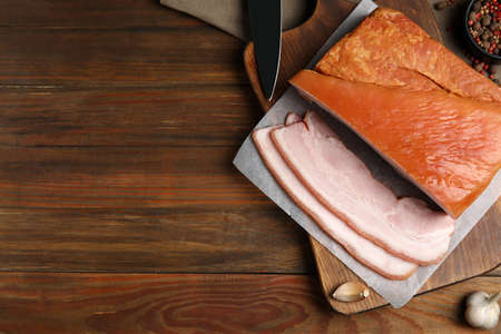 Delicious smoked bacon and garlic on wooden table, flat lay. Space for text