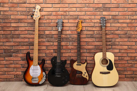 Modern electric and classical guitars near red brick wall indoors
