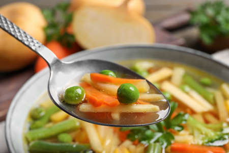 Spoon with delicious turnip soup above bowl, closeup