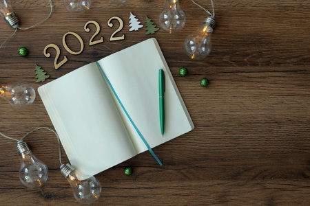 Open planner and Christmas decor on wooden background, flat lay. 2022 New Year aimsの写真素材