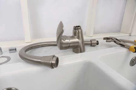 Disassembled water tap and pipe wrench near sink on countertop
