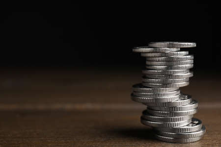 Many coins stacked on wooden table against black background, space for text