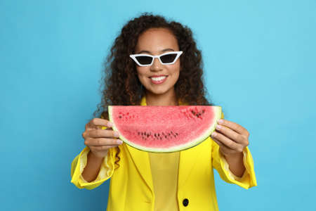 Beautiful young African American woman with watermelon against light blue background, focus on handsの写真素材