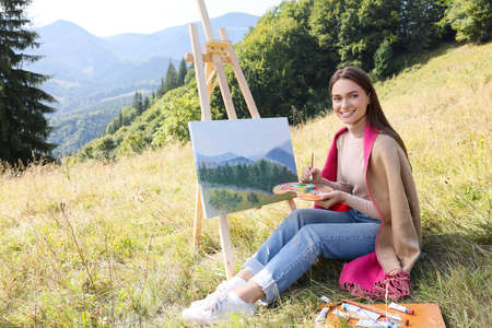 Young woman drawing on easel in mountainsの写真素材
