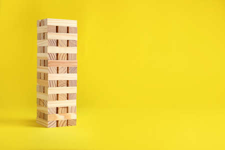 tower made of wooden blocks on yellow background, space for text