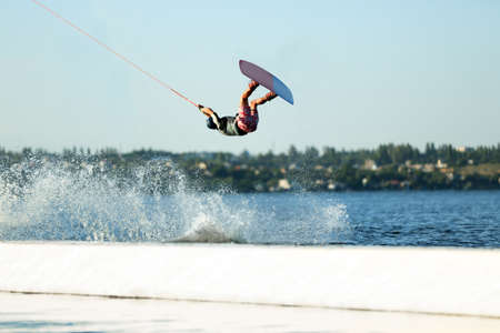 Teenage wakeboarder doing trick over river. Extreme water sport
