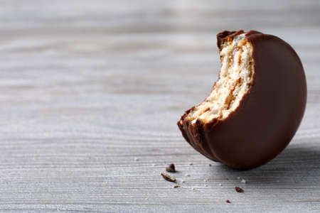 Tasty bitten choco pie on white wooden table, closeup. Space for text