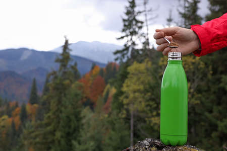 Woman pouring instant coffee into thermo bottle in mountains, closeup. Space for textの写真素材