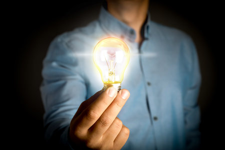 Glow up your ideas. Man holding light bulb on dark background, closeupの写真素材