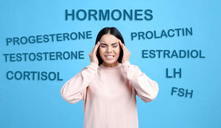 Hormones imbalance. Stressed young woman and different words on light blue backgroundの写真素材