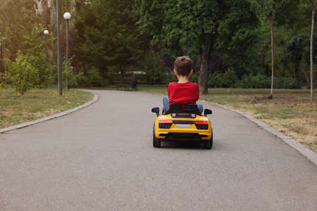 Cute little boy driving children's car outdoors, back view. Space for textの写真素材