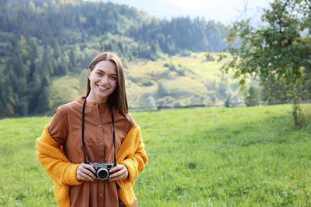 Happy woman with camera on meadow in mountainsの写真素材
