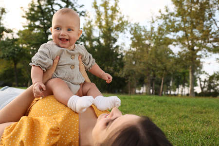 Happy mother with adorable baby lying on green grass in parkの写真素材