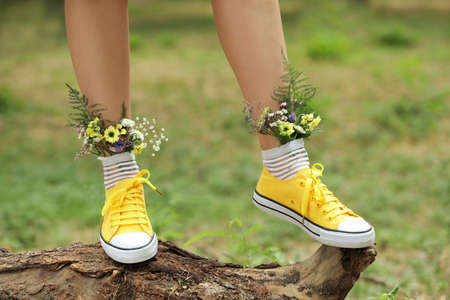 Woman standing on log with flowers in socks outdoors, closeup