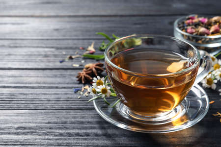 Glass cup of freshly brewed tea and chamomile flowers on black wooden table, closeup. Space for textの写真素材