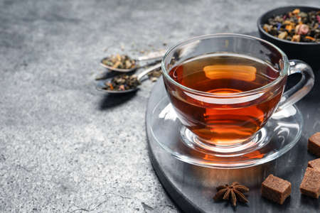 Glass cup of freshly brewed tea, dry leaves and sugar on gray table. Space for textの写真素材